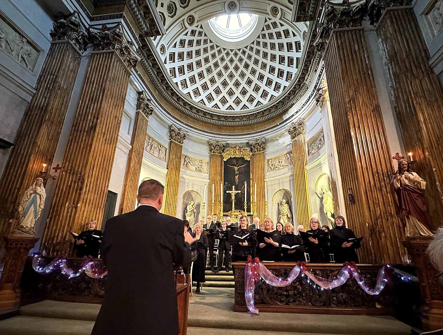 The Pocklington Singers singing carols in the Chapel of Ss Mary & Everilda, beneath the coffered dome, with their conductor in the foreground.